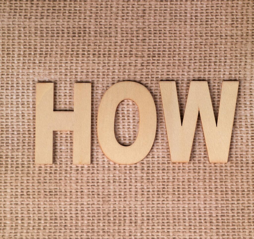 Wooden letters forming "HOW" on a burlap background, emphasizing question or inquiry.