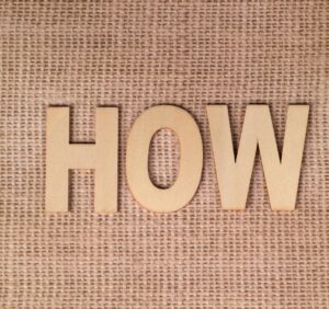 Wooden letters forming "HOW" on a burlap background, emphasizing question or inquiry.