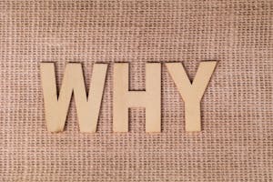 Wooden letters spelling 'WHY' on a textured burlap fabric, inviting curiosity and reflection.